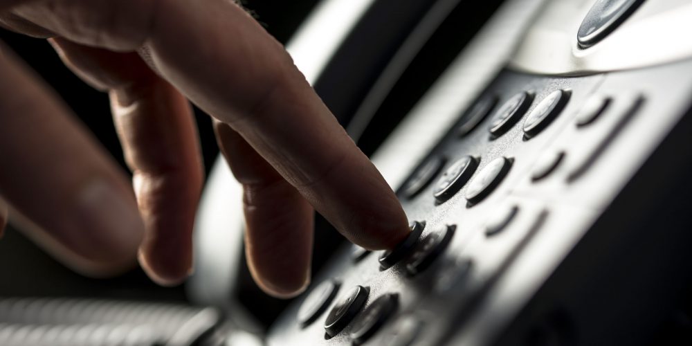Closeup view of the hand of a man making a telephone call on a desktop instrument pressing the numbers on the keypad